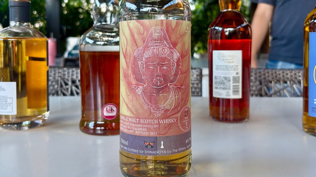 A bottle of Single Malt Scotch Whisky with a distinctive label featuring a stylized figure, surrounded by other whisky bottles on a table.