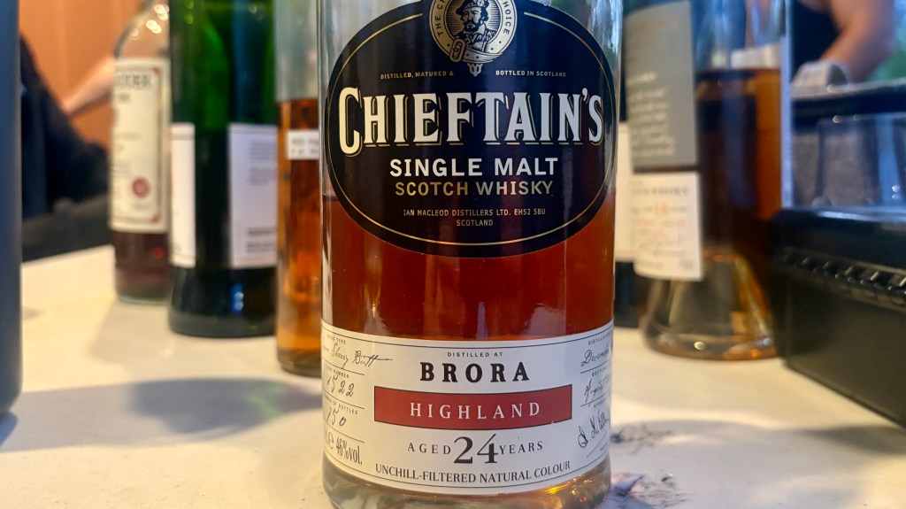 A bottle of Chieftain's Single Malt Scotch Whisky, aged 24 years, from Brora, Highland, displayed on a table with other liquor bottles in the background.