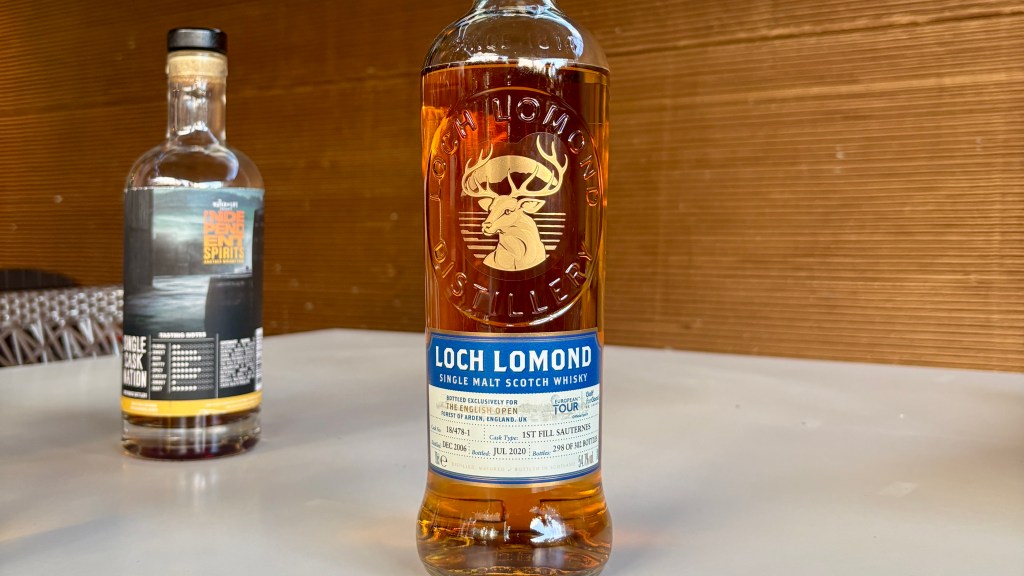 A bottle of Loch Lomond single malt Scotch whisky with a distinctive label featuring a deer logo, placed in the foreground. Another bottle of independent spirits is slightly blurred in the background.